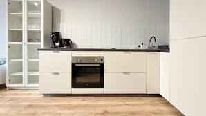 Una cocina moderna con armarios blancos, horno integrado, cafetera y salpicadero con estampado de espiga.