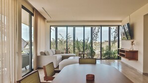 Un salón moderno con una gran mesa de comedor, asientos cómodos, un televisor montado en la pared y vistas a zonas verdes y edificios a través de amplios ventanales.