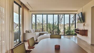 Un salón moderno con una gran mesa de comedor, asientos cómodos, un televisor montado en la pared y vistas a zonas verdes y edificios a través de amplios ventanales.