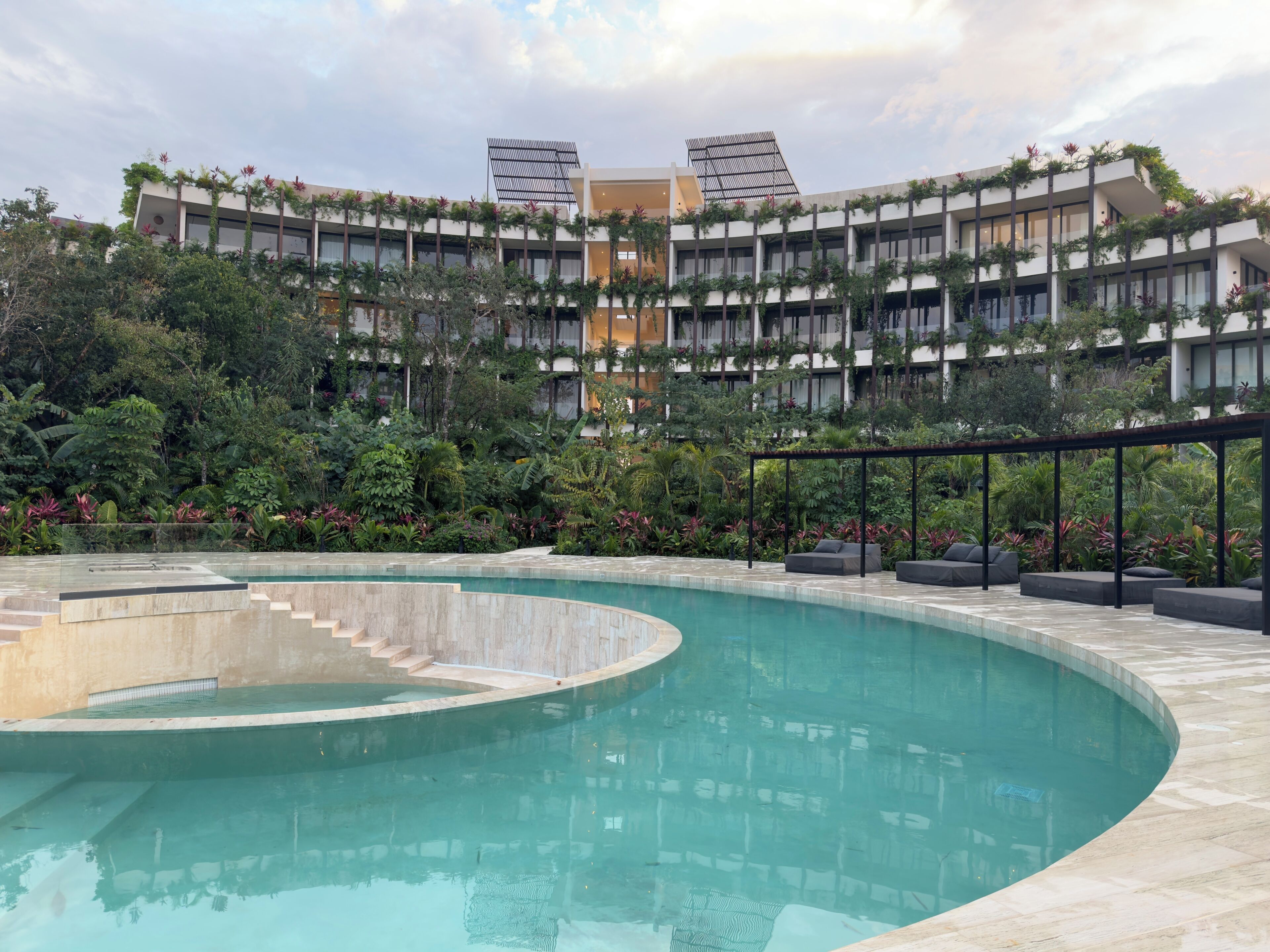 Un hôtel moderne doté d’une grande piscine extérieure, entouré d’une végétation luxuriante et d’un immeuble à plusieurs étages avec des balcons.
