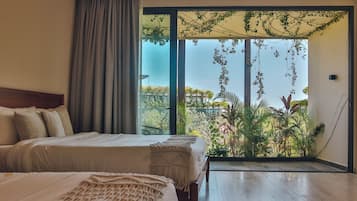 Un dormitorio con dos camas, un amplio ventanal corredera que da a un balcón con plantas y vistas a edificios.