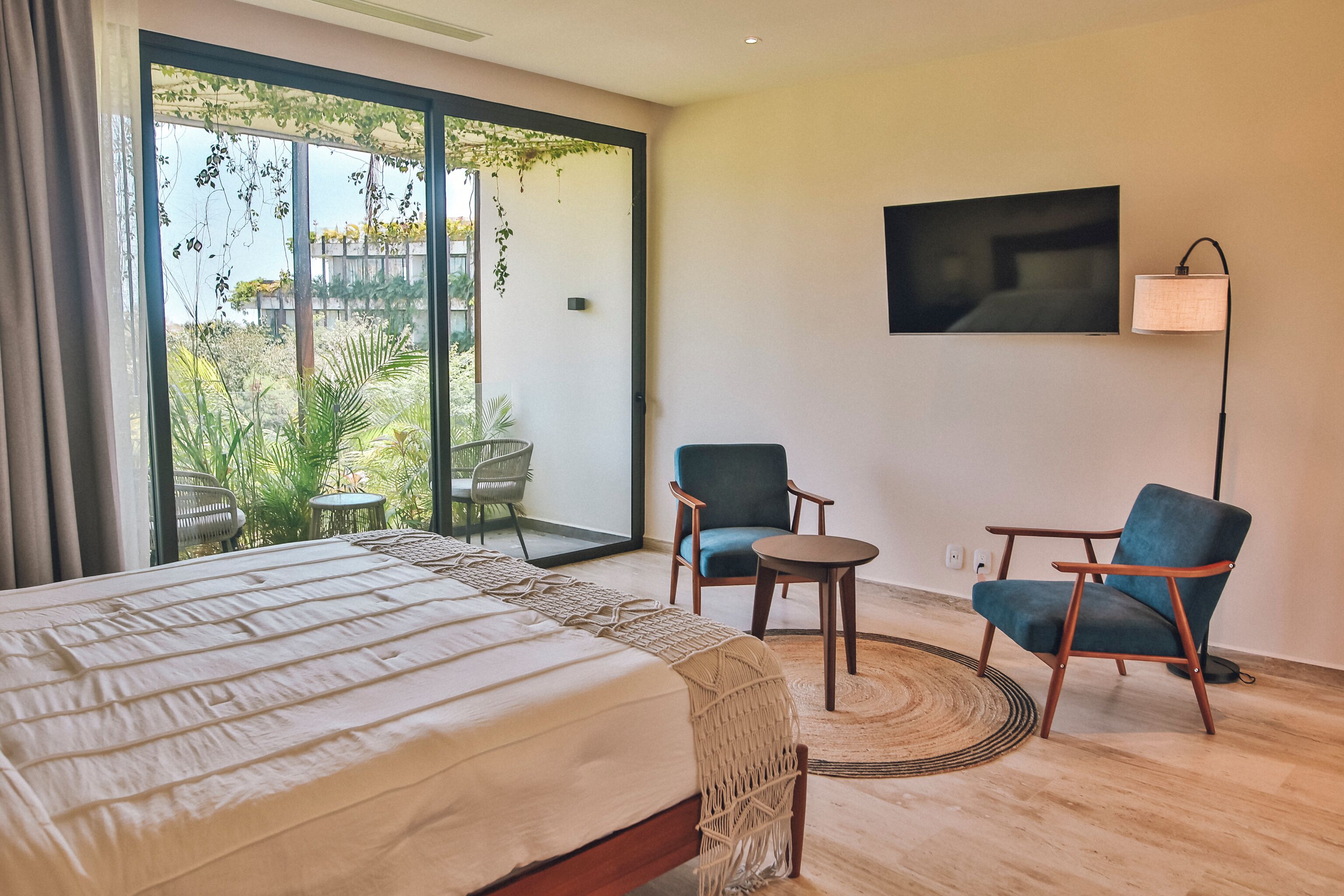Ein Hotelzimmer mit einem Bett, zwei Sessel, einem kleinen Tisch, einem Fernseher und Blick auf Grünfläche.