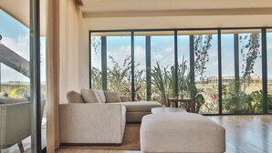 Una sala de estar moderna con un sofá seccional, un pequeño reposapiés y vistas a un exuberante jardín a través de grandes ventanales.