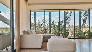 Una sala de estar moderna con un sofá seccional, un pequeño reposapiés y vistas a un exuberante jardín a través de grandes ventanales.
