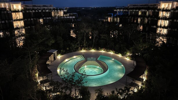 Una piscina circular rodeada por una terraza de madera, con edificios al fondo.