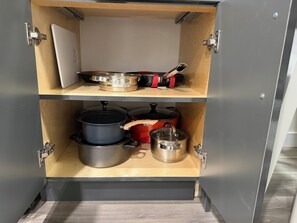 Ein Küchenschrank mit zwei Einlegeböden, auf denen Kochgeschirr und ein Schneidebrett liegen.