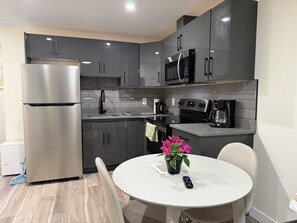 A modern kitchen with grey cabinets, stainless steel appliances, and a round dining table with a potted plant. - Dykee Morden 2-bed, 1-bath suite in The Greens, just 4 min from Everyday kitchen (Regina)
