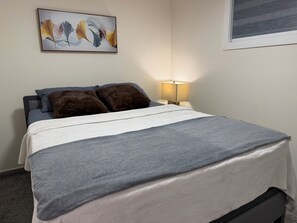 A neatly made bed with a grey and white duvet, two dark brown pillows, and a wall-mounted abstract painting. - Dykee Morden 2-bed, 1-bath suite in The Greens, just 4 min from Everyday kitchen (Regina)