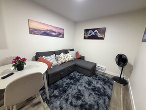 Ein modernes Wohnzimmer mit einem Ecksofa, einem Esstisch, einer Zimmerpflanze und Kunstwerken an den Wänden.