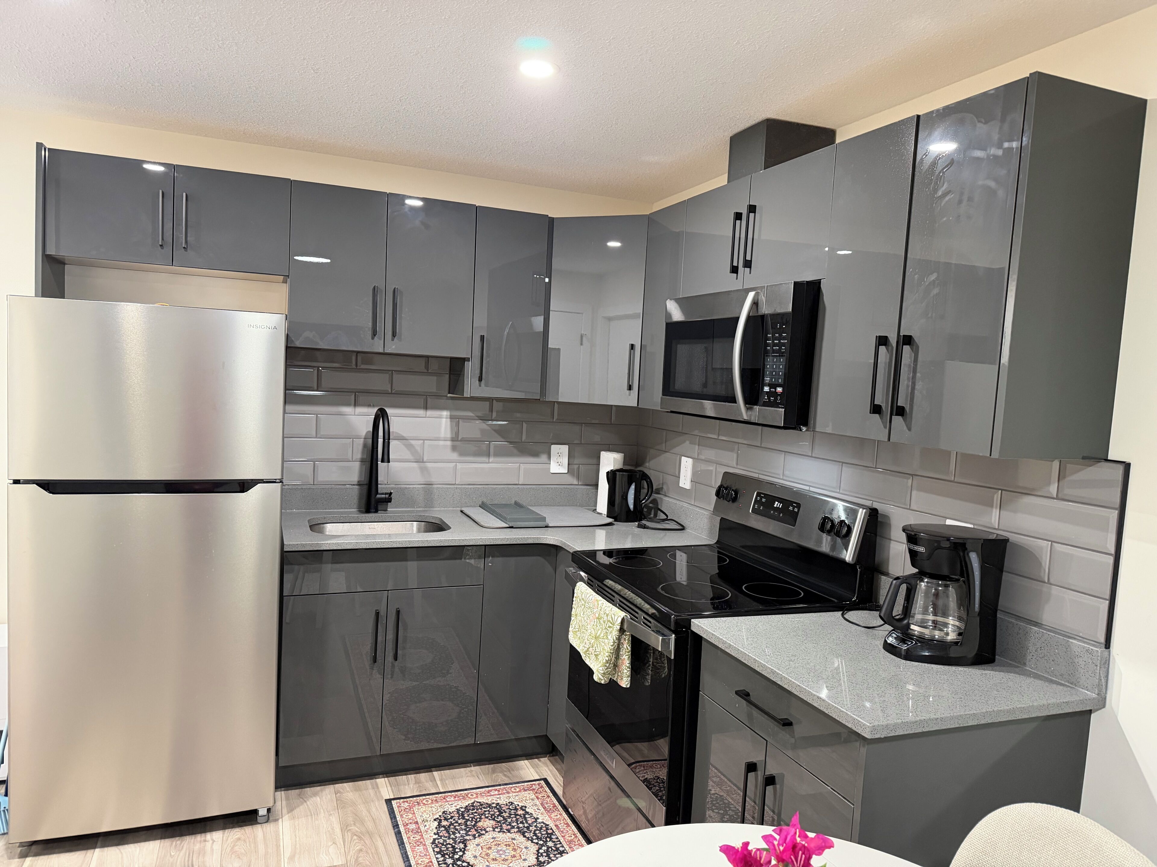 A modern kitchen with stainless steel appliances, grey cabinets, and a black microwave.