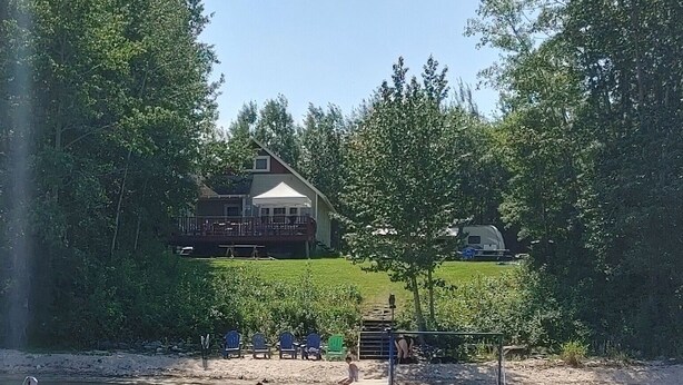 Une propriété au bord du lac comprenant une maison, un quai et un espace extérieur aménagé pour s’asseoir.