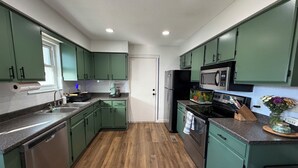 Una cocina con gabinetes verdes, electrodomésticos de acero inoxidable, piso de madera y una ventana.