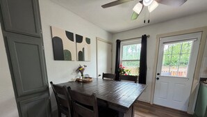 Un comedor con una mesa de madera, sillas, un ventilador de techo y una ventana con cortinas.