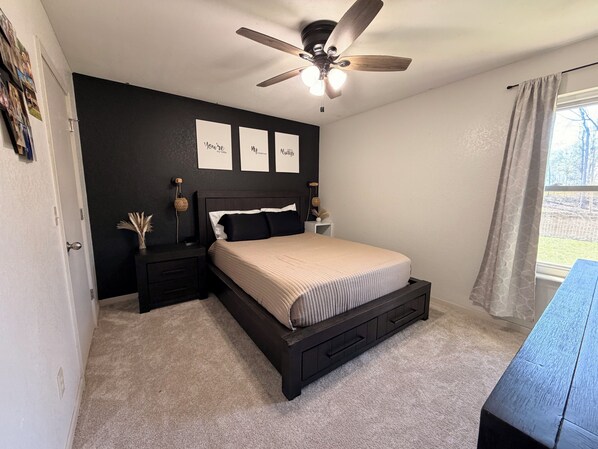 A bedroom with a bed, nightstands, a ceiling fan, and a window with curtains.