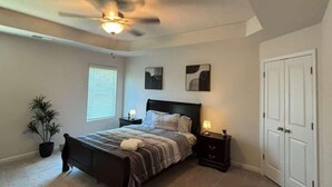 Un dormitorio con cama, mesitas de noche, ventilador de techo, ventana y puerta.
