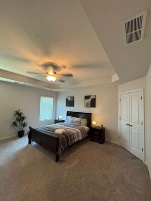 A bedroom with a bed, bedside tables, a ceiling fan, a window, and a door. - Spacious 3-bedroom townhome in charming Oakwood (Oakwood)