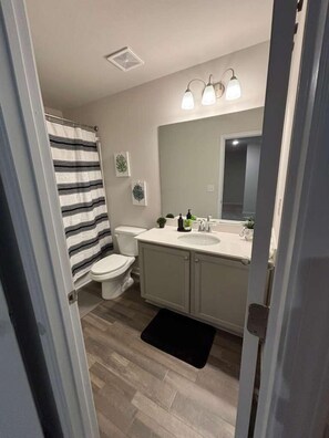 A bathroom with a toilet, a sink, a mirror, and a shower curtain. - Spacious 3-bedroom townhome in charming Oakwood (Oakwood)