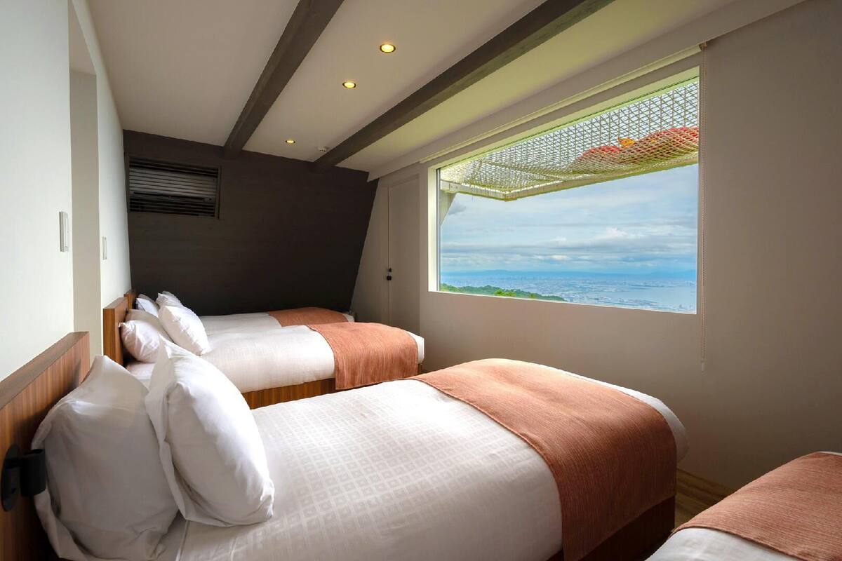 A hotel room with two beds, a large window with a view, and a ceiling with exposed beams and recessed lighting.