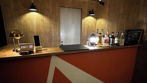 Un comptoir d’accueil en bois, sur lequel se trouvent un ordinateur portable, une horloge numérique, une lampe et diverses bouteilles.