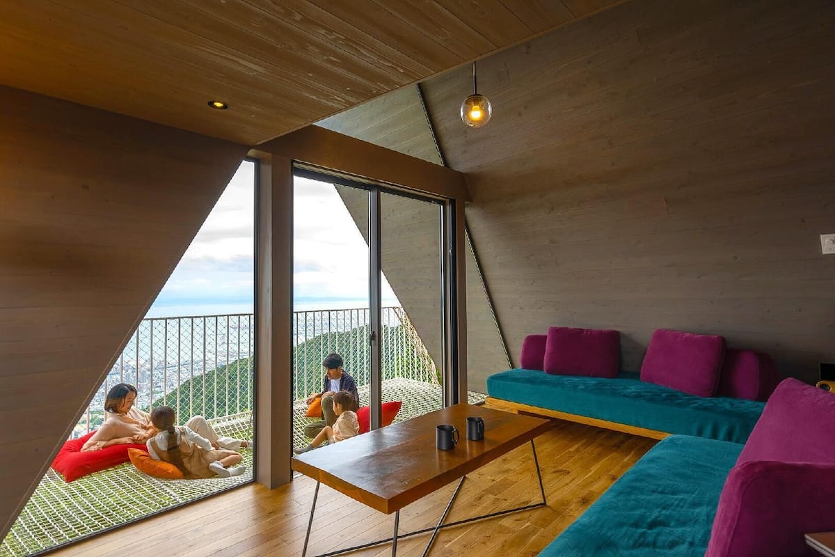 A modern interior with a wooden ceiling, large windows, a wooden table, and a teal sofa with purple cushions.