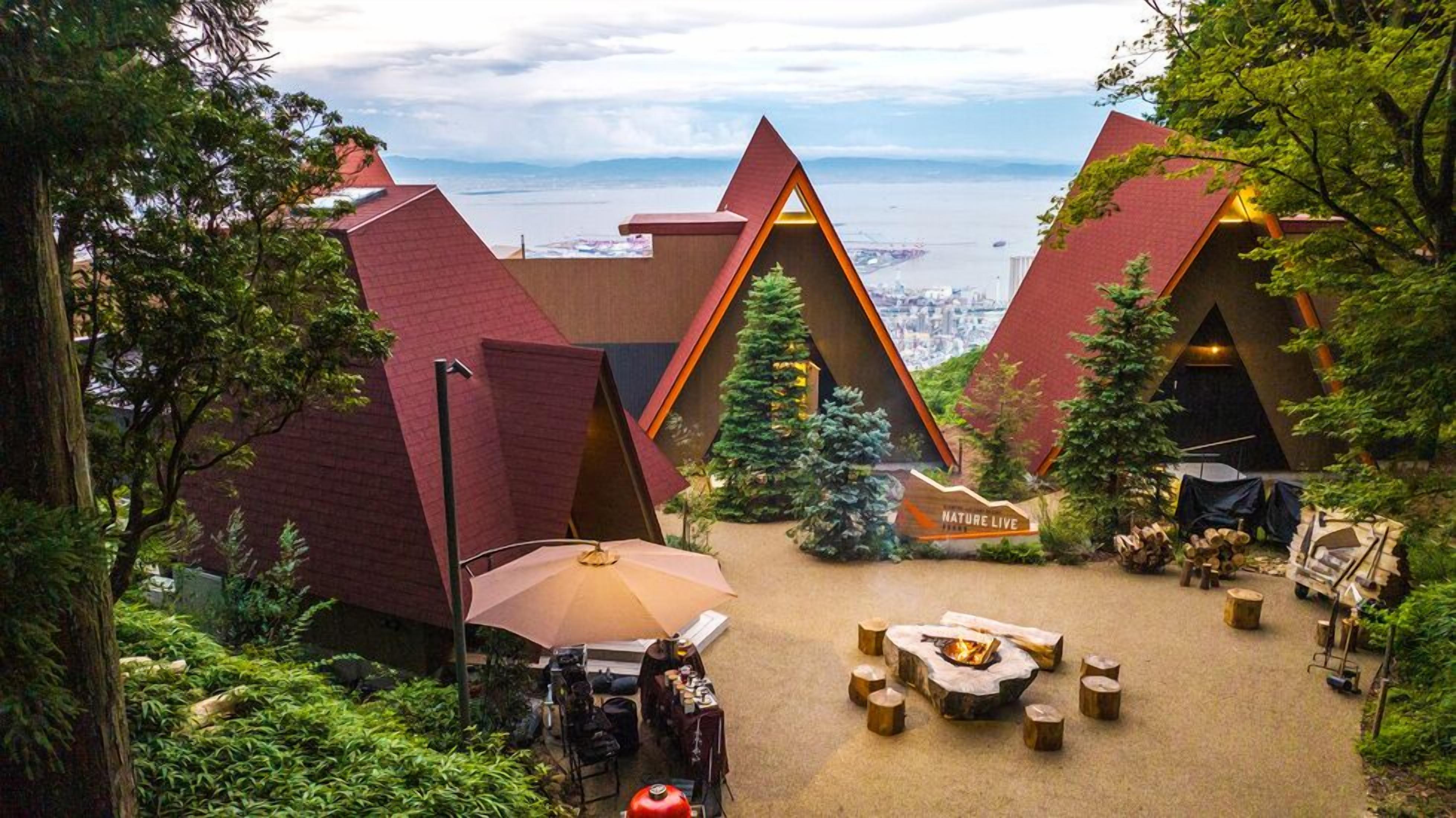 A nature-themed lodge with triangular roofs, a central fire pit, and a view of a cityscape.
