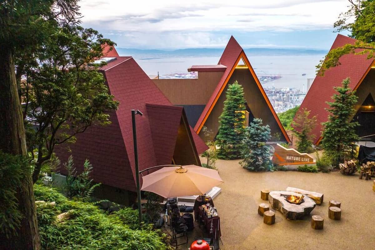 A nature-themed lodge with triangular roofs, a central fire pit, and a view of a cityscape.