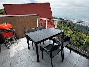 Un patio con mesa y sillas, una parrilla y vistas a un paisaje urbano y montañas.