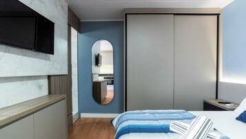 Un dormitorio con una cama, un televisor montado en la pared, un espejo y un armario.