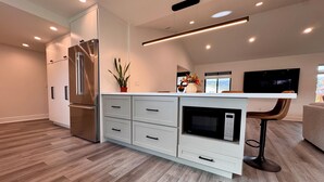 A modern kitchen with a built-in microwave, a stainless steel refrigerator, and a flat-screen TV mounted on the wall. - New, Quiet, Modern Comfort 3-bedroom house in tranquil Cupertino (Cupertino)