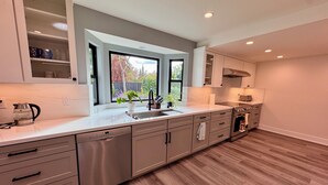 A modern kitchen with a dishwasher, sink, and stove. There is a window with a view of trees and a potted plant on the counter. - New, Quiet, Modern Comfort 3-bedroom house in tranquil Cupertino (Cupertino)