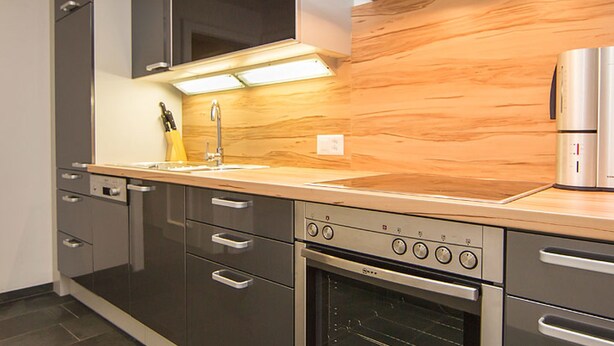 Eine moderne Küche mit dunklen Schränken, einem Edelstahlbackofen und einer Holzrückwand.