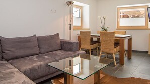 Ein modernes Wohnzimmer mit einem Glastisch, einem grauen Sofa, Korbstühlen und einem Esstisch.