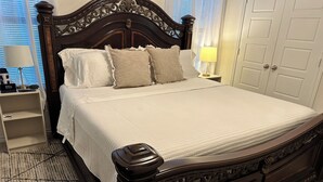 Een net opgemaakt bed met een houten hoofdbord, een nachtkastje met een lamp en een nachtkastje met een klok.