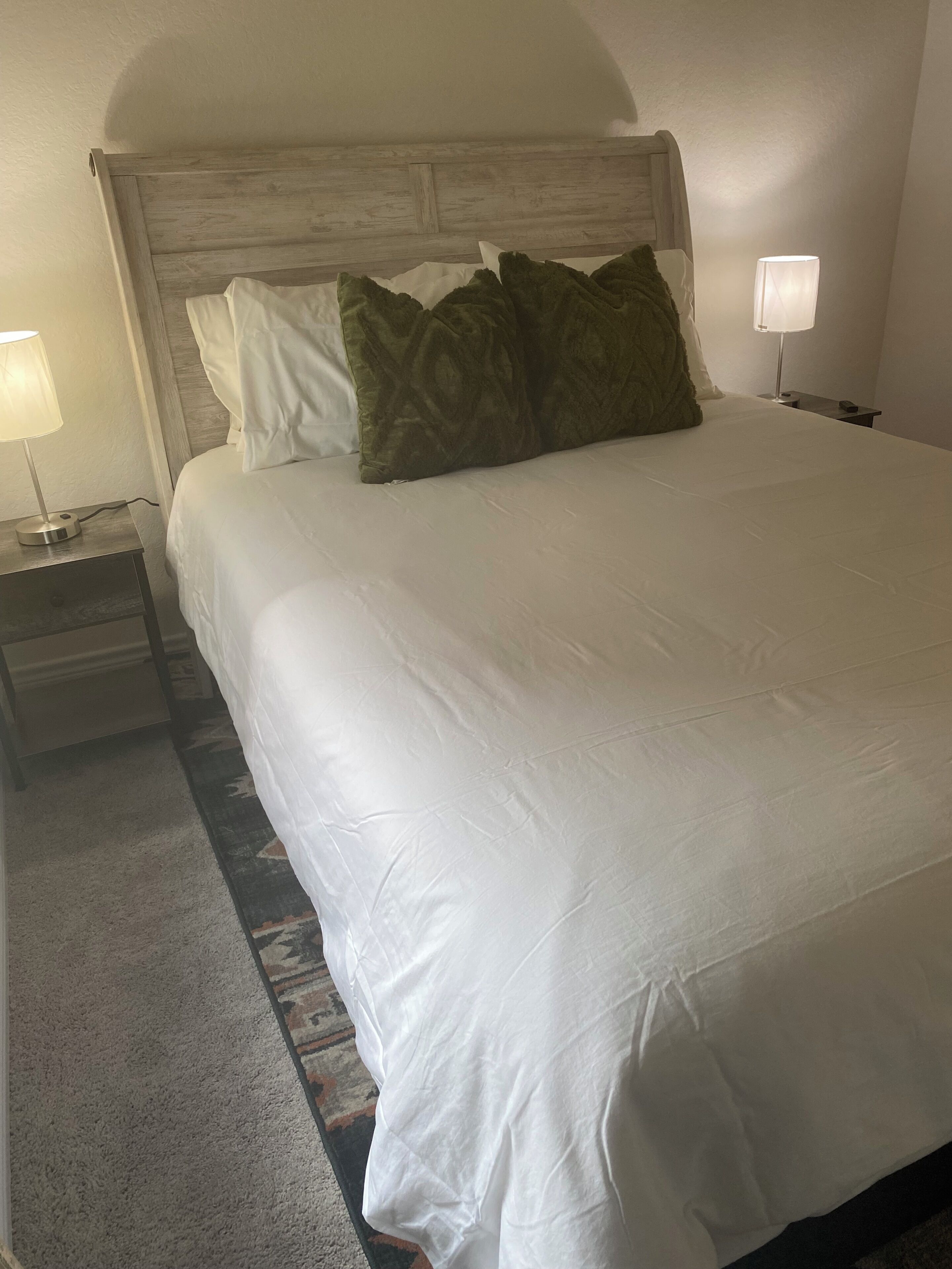 A hotel room with a large bed, two bedside lamps, a headboard, and a carpeted floor.
