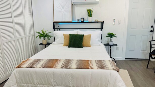 A neatly arranged bedroom with a bed, bedside tables, a mirror, and a door. -  Functional and newly renovated in-law suite with private entrance and yard (Sanford)