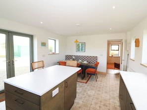 A modern kitchen with a dining area, featuring a central island, built-in cabinets, and a seating area with a patterned bench. - KNOCKNANUSS, family friendly in Ballinascarty, County Cork (Unknown)