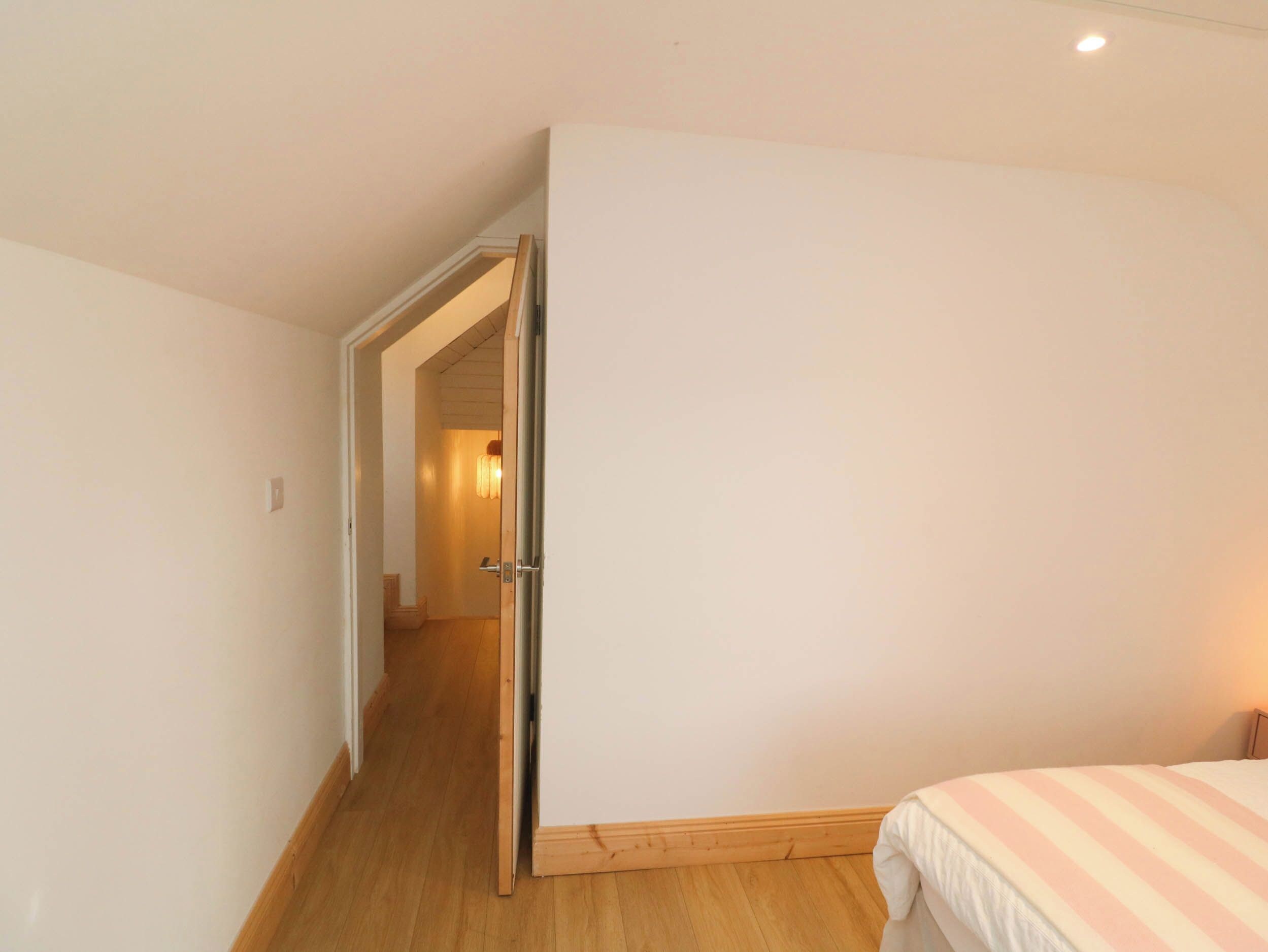 A narrow hallway leading to a bedroom with a bed and a door.
