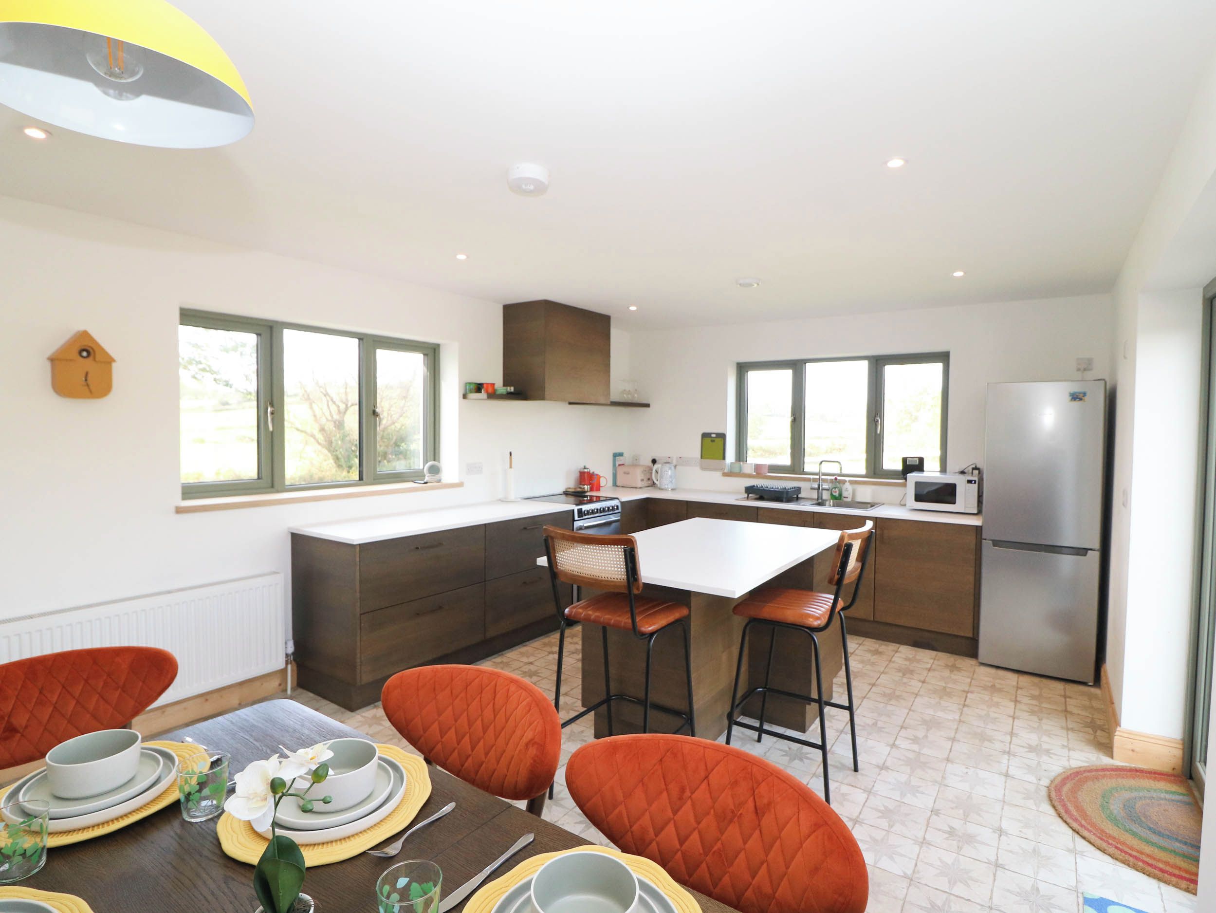 A modern kitchen with a dining area, featuring a central island, bar stools, and a refrigerator.