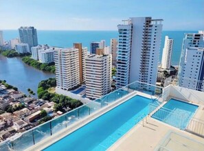Ein Hochhaus mit Pool auf dem Dach, umgeben von weiteren Gebäuden und einem Gewässer.