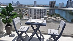 A balcony with two chairs and a table, overlooking a cityscape with high-rise buildings and a river. - Spacious 3-bedroom condo in delightful Cartagena with AC and gym (Cartagena)