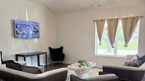 A living room with two sofas, a coffee table, a TV mounted on the wall, a ceiling fan, and a window with curtains. - Fantastic 4BR Houston Chalet Near NRG, TSU, UofH, & Medical Center (Houston)