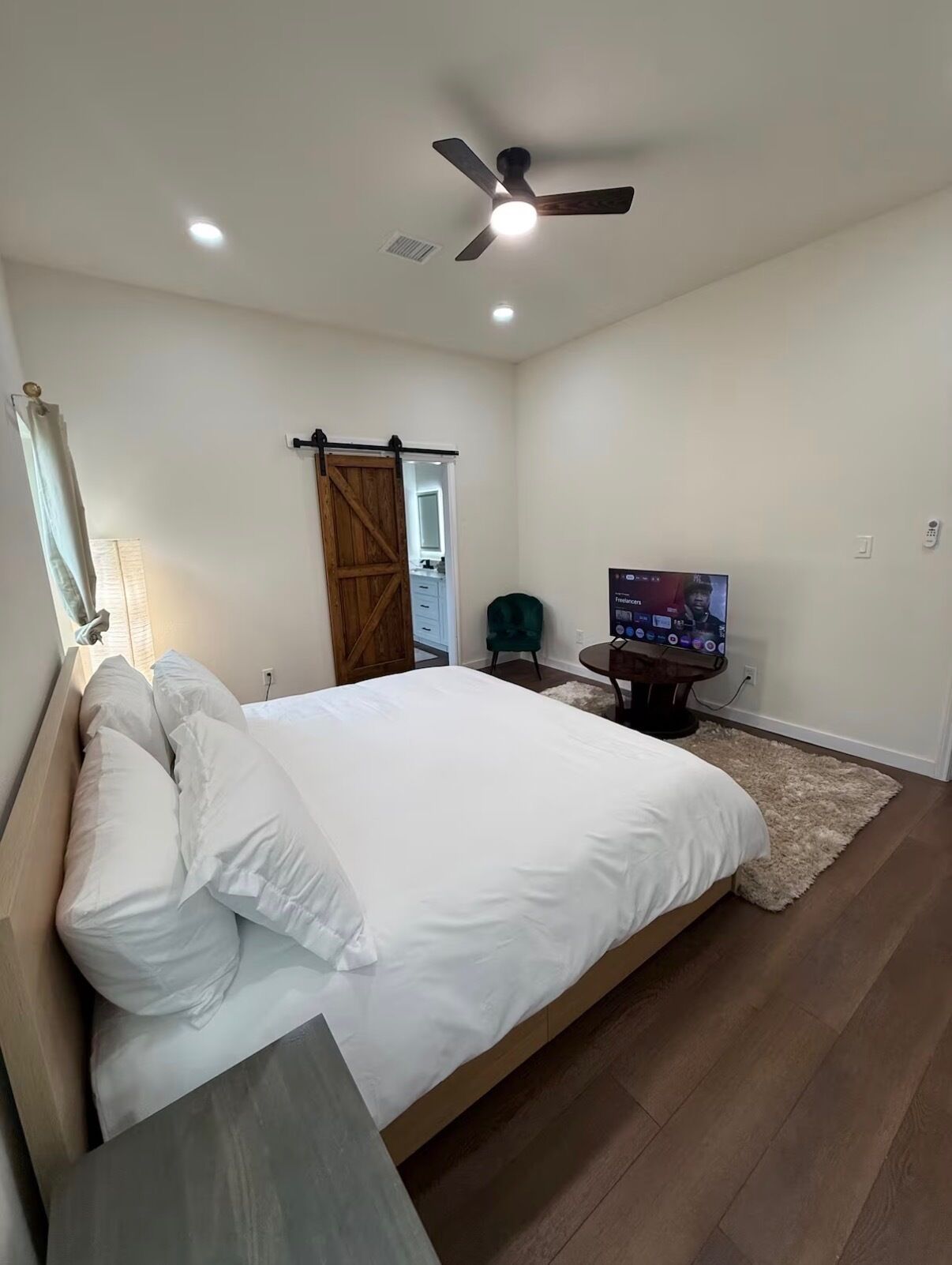 Een slaapkamer met een bed, een plafondventilator, een televisie en een deur naar een andere kamer.
