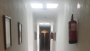 Un couloir au sol carrelé, avec des tableaux encadrés accrochés aux murs et un extincteur fixé au mur de droite.