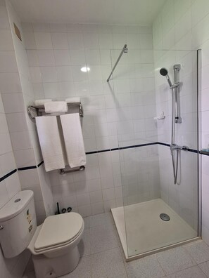 A bathroom with a toilet, a shower with a glass door, and two towels hanging on a rack. - Hotel Portugal (Lepe)