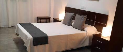 Una habitación de hotel con una cama grande, mesitas de noche, una silla, un cuadro con una vista urbana y una cortina.