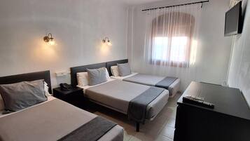 A hotel room with two beds, a desk, a TV, and a window with curtains.