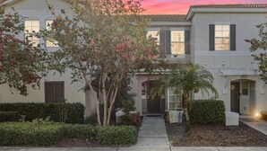 A two-story residential building with a front entrance, a small driveway, and a well-maintained garden with various plants and trees. - Sunny Poolside Escape (Kissimmee)
