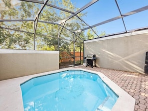 Ein Pool mit Glasveranda, ein Grill und eine Terrasse mit Ziegelsteinen.