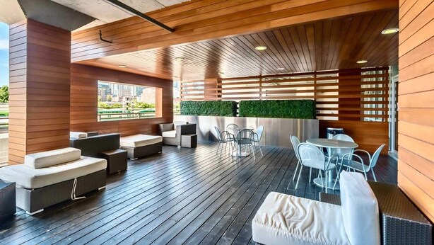 Ein moderner Außen-Loungebereich mit Holzboden, weiß gepolsterten Sitzgelegenheiten und einer grünen Heckenwand.