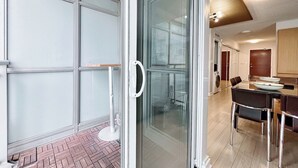 Ein modernes Interieur mit Glastür zum Balkon, einem Essbereich mit Tisch und Stühlen sowie einer im Hintergrund sichtbaren Küche.